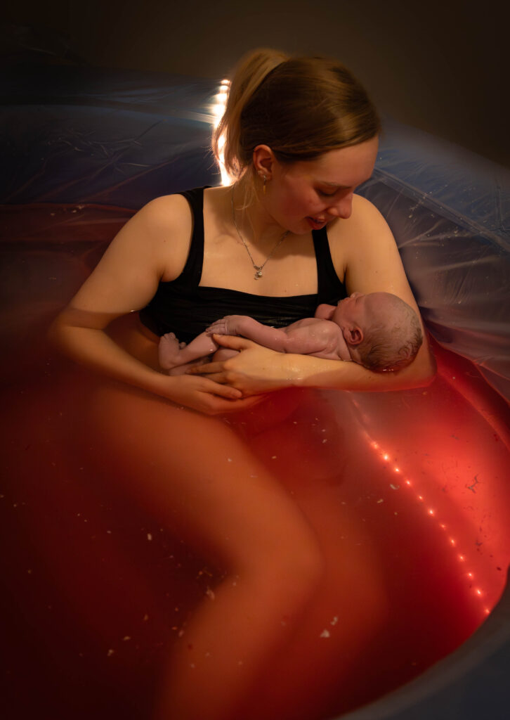 Moeder met pasgeboren kindje op haar arm in een bevallingsbad.